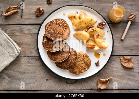 Herbstfrühstück - Pfannkuchen mit karamellisierten Äpfeln, Pekannüssen und Honig auf Holztisch, Draufsicht, Kopierraum. Gesunde vegetarische Mahlzeit der Saison. Stockfoto