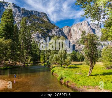 Ein Kind spielt im Wasser des Merced River, der durch das Yosemite Valley fließt und die Felswände bilden eine großartige Kulisse. Stockfoto