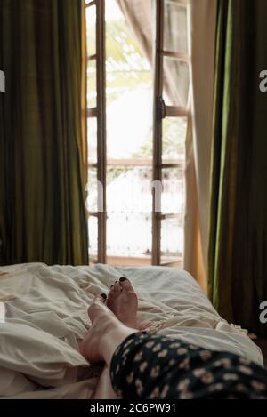 Frau, die sich auf einem Bett entspannt und durch die Fenstertüren auf einen Balkon in Marrakesch, Marokko blickt. Stockfoto