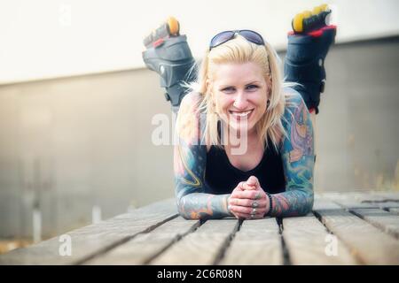 Blonde tätowierte Frau mit Rollerklingen Stockfoto
