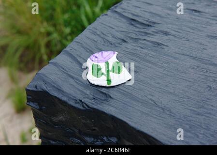 Handbemalte Muschel mit Blumen-Design auf einer schwarzen, glänzenden Stahloberfläche. Stockfoto