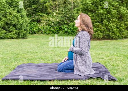 Glücklich schwangere kaukasische Frau entspannen in einem Park mit den Händen auf ihrem Bauch. Stockfoto