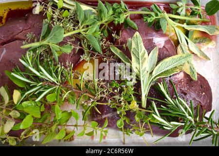 Wildschwein marinierte Steaks in Olivenöl und Auswahl an frischen Gartenkräutern. Salbei Oregano Thymian süßer Majoran und Minzzweige leicht würzen rotes Fleisch Stockfoto