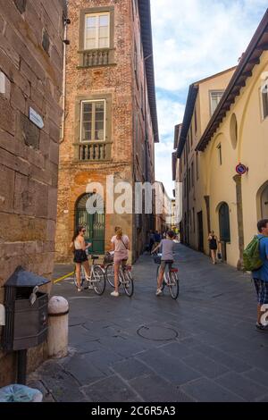 Lucca, Italien - 14. August 2019: Mädchen auf dem Fahrrad in der alten engen mittelalterlichen Straße mit Café und Geschäften im historischen Zentrum von Lucca, Toskana Stockfoto