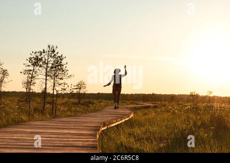 Silhouette der Frau mit Rucksack auf Wanderweg im Sommer im Freien. Naturforscher genießt die Natur und einen Moment bei Sonnenuntergang zu Fuß auf dem Weg durch Torfmoor Stockfoto