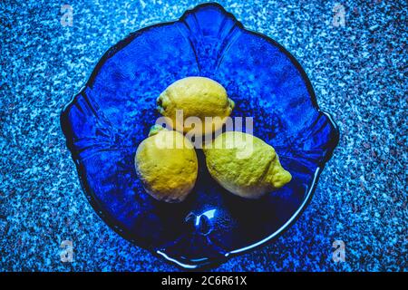 Drei gelbe Zitronen in einer großen blauen Glasschale Stockfoto