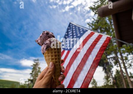 Frau Hand hält ein Waffeleisen-Eis mit einer amerikanischen Flagge weht in den Hintergrund. Patriotisches Foto Stockfoto
