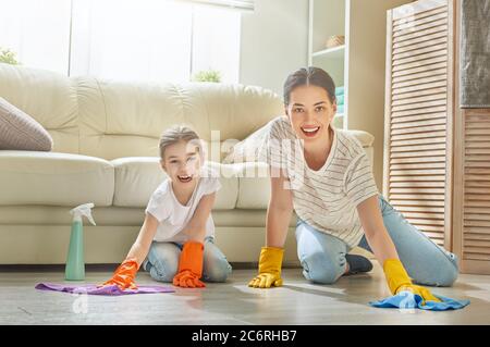 Glückliche Familie putzt das Zimmer. Mutter und Tochter machen die Reinigung im Haus. Eine junge Frau und ein Mädchen stauben. Netter kleiner Helfer. Stockfoto