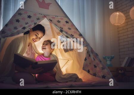 Familie Schlafenszeit. Mutter und Kind Tochter lesen ein Buch im Zelt. Ziemlich junge Mutter und schönes Mädchen mit Spaß im Kinderzimmer. Stockfoto