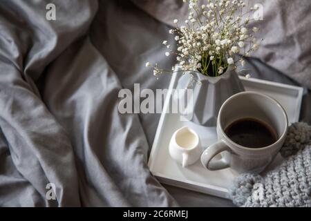 Gemütliches Frühstück im Bett, Tasse Kaffee und Milch auf dem grauen Stoff, Platz für Text. Frühstück im Bett. Stockfoto