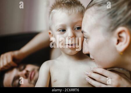 Mutter spricht mit dem kleinen Sohn, während der Vater sie im Zimmer ansieht. Familienportrait. Frohe Familie Stockfoto