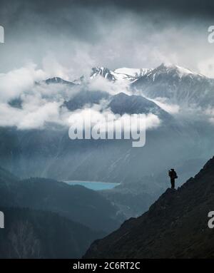 Wanderer in Silhouette steht auf dem Felsen in der schönen Berglandschaft mit See und verschneiten Gipfeln Stockfoto