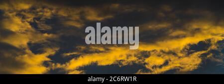 Panorama goldene flauschige Wolken von verschwindenden Strahlen bei Sonnenuntergang und dunklen Cumulonimbus schwebend über blauen Himmel, Saison Wetter zu ändern beleuchtet Stockfoto