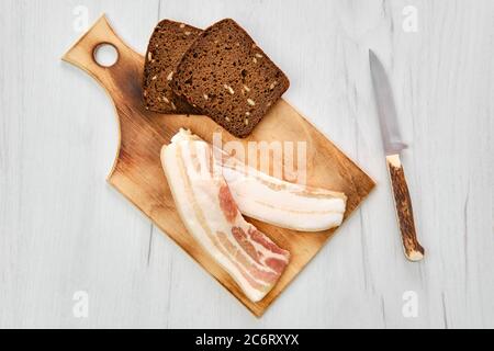 Von oben aus gesehen zwei Scheiben Speck und braunes Brot auf einem Holzschneidebrett Stockfoto