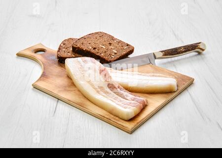 Von oben aus gesehen zwei Scheiben Speck und braunes Brot auf einem Holzschneidebrett Stockfoto