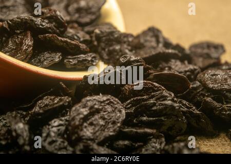Getrocknete Pflaumen in einer Keramikschale und getrocknete Pflaumen auf einem Hintergrund von grobstrukturiertem Quappen verstreut. Nahaufnahme Stockfoto