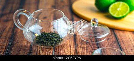 Eine Glas Teekanne mit Teeblättern innen auf einem Holztisch. Stockfoto