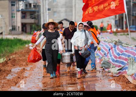 (200712) -- POYANG, 12. Juli 2020 (Xinhua) -- Freiwillige tragen Mungbohnensuppe für bewaffnete Polizisten, um sich bei heißem Wetter im Dorf Jiangjialing, Stadt Poyang, Provinz Jiangxi, im Osten Chinas, abzukühlen, 11. Juli 2020. Aufgrund der anhaltenden starken Regenfälle erhöhte die ostchinesische Provinz Jiangxi ihre Reaktion auf die Überschwemmungskontrolle innerhalb von nur drei Tagen von Stufe III auf Stufe I. Neben Parteimitgliedern der Kommunistischen Partei Chinas (KPCh) und bewaffneten Polizisten, die organisiert sind, um am Kampf gegen die Flut teilzunehmen, widmet sich auch eine freiwillige Gruppe älterer Frauen im Dorf Jiangjialing ihren Bemühungen. Yu Fengy Stockfoto