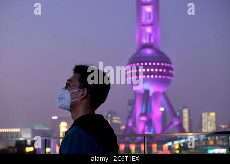 Junger Mann trägt OP-Maske mit Blur Oriental Pearl TV Tower in der Nacht Stockfoto