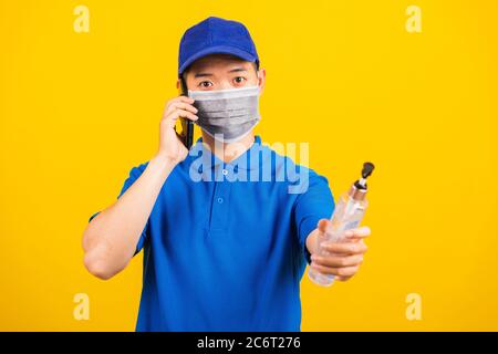 Asiatische junge gut aussehende Lieferung Mann trägt Gesichtsmaske schützende halten Alkohol Desinfektionsgel und Anruf an Kunden von Handy Studio Schuss isolieren Stockfoto