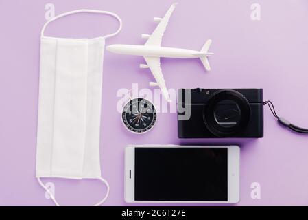 Welttourismustag, Ansicht von oben von minimalem Modellflugzeug, Flugzeug, Seesterne, Kompass, Smartphone leerer Bildschirm und Gesichtsmaske isoliert auf violettem Hintergrund, Stockfoto