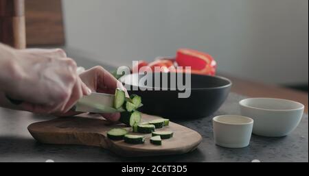 Mann hackt Gurke auf Olivenholz Brett für griechischen Salat Stockfoto