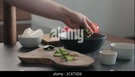 Mann hackt Gurke auf Olivenholz Brett für griechischen Salat Stockfoto