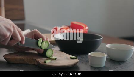 Mann hackt Gurke auf Olivenholz Brett für griechischen Salat Stockfoto