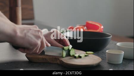 Mann hackt Gurke auf Olivenholz Brett für griechischen Salat Stockfoto