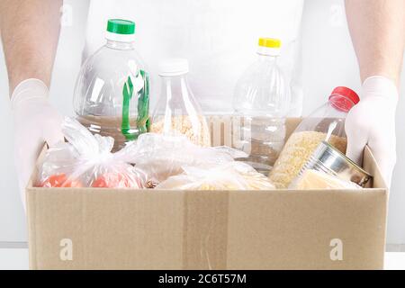 Freiwillige in Handschuhen und Maske mit Spendenbox mit Lebensmitteln auf grauem Hintergrund. Stockfoto