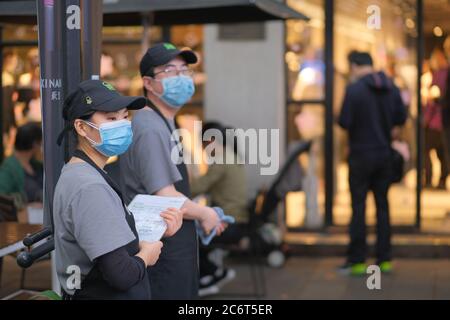 Das Restaurantpersonal trägt eine Gesichtsmaske, um das Covid-19 Coronavirus zu vermeiden, und steht vor dem Restaurant. Verwischen Sie den Hintergrund des Kunden Stockfoto