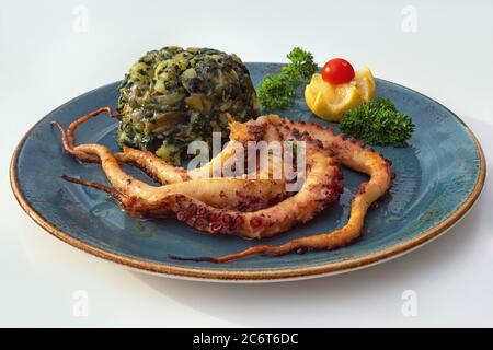 Balkan-Küche. Teller mit gegrilltem Oktopus und grünem Blattgemüse auf weißem Tisch. Freier Speicherplatz für Text Stockfoto