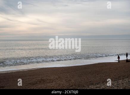 Zwei Leute beobachten EINEN Paddlebarder im frühen Abendlicht vor der Küste in Brighton, East Sussex, Großbritannien Stockfoto