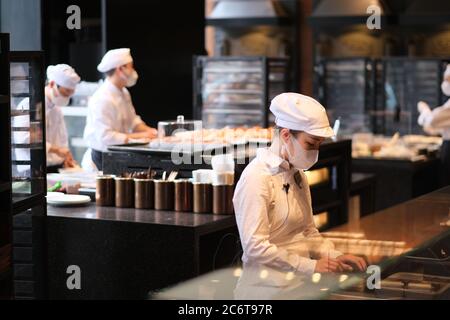 Angestellte tragen Gesichtsmaske, um covid-19 Coronavirus zu vermeiden, arbeiten in der Bäckerei Stockfoto