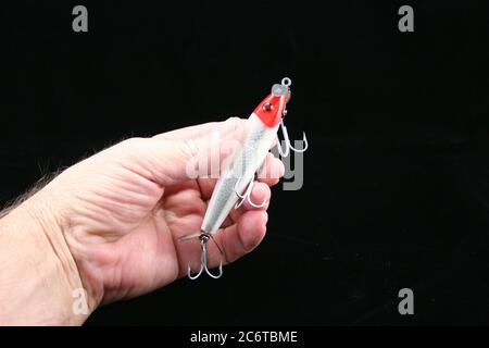 Schwarzer Hintergrund der Hand des alten Mannes hält Angelköder mit Haken Stockfoto