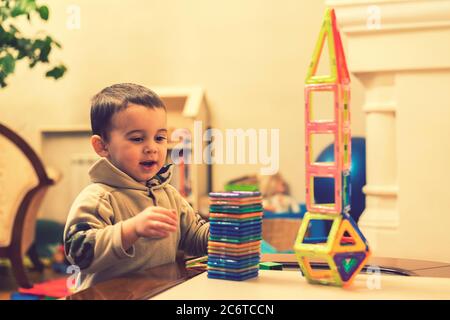 Der Junge 2 Jahre bauen einen Turm von einem hellen Konstrukteur. Kleine lächelnde Junge spielt mit magnetischen Konstruktor Spielzeug. Junge spielen intellektuelle Spielzeug Stockfoto