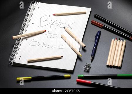 Flache Ansicht eines weißen Notizbuchs, Farbstifte, blauer Stift auf einem Tisch vor schwarzem Hintergrund. Vorbereitung auf eine Schule. Zurück zur Schule. Stockfoto