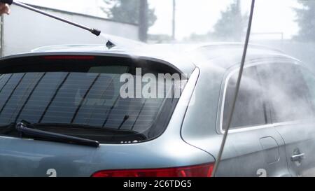 Selbstbedienungswaschanlage. Waschen eines Autos in einer Autowäsche mit einer Hochdruckspritze. Graues Auto. Einsparkonzept Stockfoto