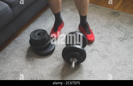Mann, der in der Nähe einer einstellbaren Hantel mit Tellern zu Hause steht. Stockfoto