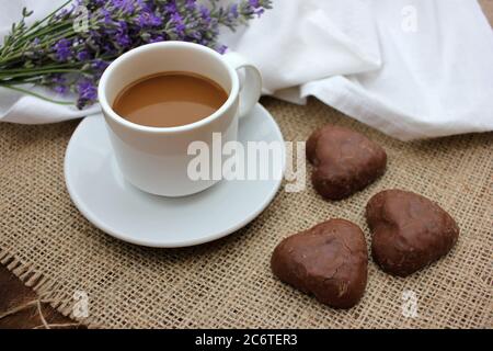Tasse Kaffee mit Lavendelblüten und herzförmigen Schokoladenkeksen auf Quaderlappen-Textur. Draufsicht Stockfoto