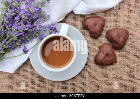 Tasse Kaffee mit Lavendelblüten und herzförmigen Schokoladenkeksen auf Quaderlappen-Textur. Draufsicht Stockfoto