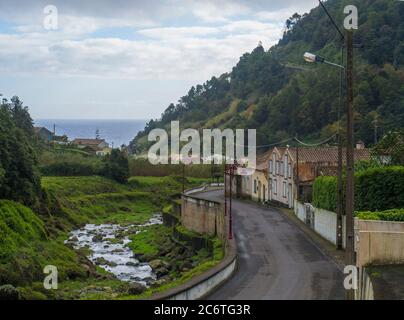 Straße im alten kleinen Dorf Faial da Terra mit kaskadierenden Fluss und Meereshorizont, Sao Miguel, Azoren Stockfoto