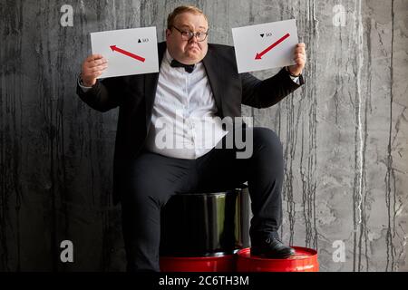 Fat kaukasischen Öl Geschäftsmann ist in verzweifelten, unglücklichen männlichen sitzt auf Öl Barrel isoliert. Der Mensch missversteht Stockfoto