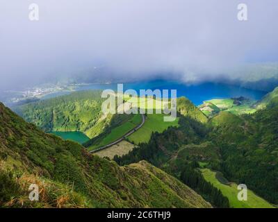 Atemberaubende Aussicht auf vulkanische Seen. Grüne Lagoa de Santiago und blaue Lagoa Azul mit Sete Cidades Dorf, teilweise von Nebel und Wolken bedeckt. Sao Stockfoto