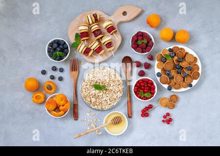 Köstlicher Frühstückstisch mit Mini-Pfannkuchen, frischen Beeren, Sommerobst, Pfannkuchenspieße, Honig und Haferbrei von oben. Gesunde Ernährung Konzept Stockfoto