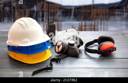 Arbeitsschutzausrüstung. Industrielle Schutzausrüstung auf Holztisch, verwischen Baustelle Hintergrund. Hüte, Ohrenschützer, Atemschutzmaske, Stockfoto