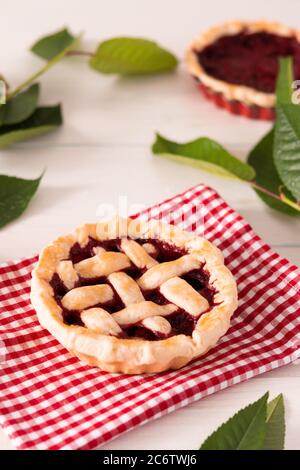 Offener Kuchen aus Mürbeteig mit Kirschen und Himbeeren, ein Kuchen mit Serviette auf weißem Hintergrund Stockfoto