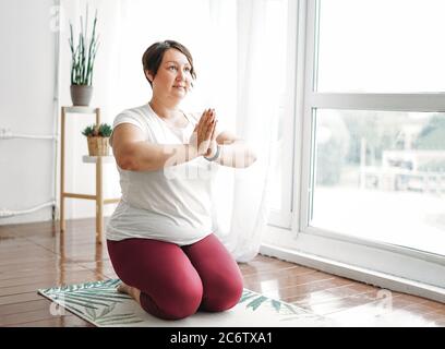 Erwachsene charmante Brünette Frau plus Größe Körper positive Praxis Yoga im hellen Studio Stockfoto