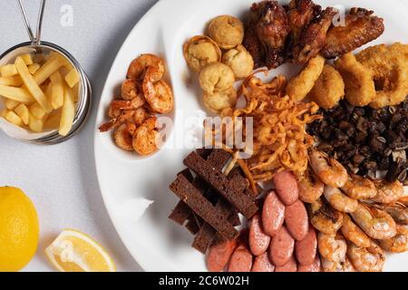 Gebratene Zwiebelringe, panierter Tintenfisch, knusprige Kartoffeln, Zitrone und gegrillte Würstchen Stockfoto