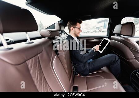 Junger Geschäftsmann mit seinem digitalen Tablet in Luxuswagen Stockfoto